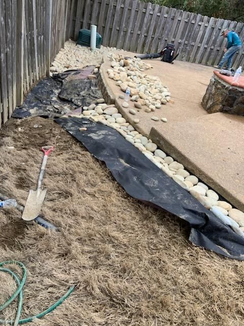 Construction site: Landscaping with rocks, fabric, dirt and two people working.