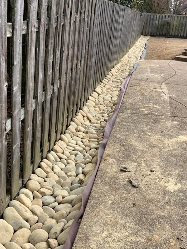 Gravel bed along a wooden fence and concrete walkway.
