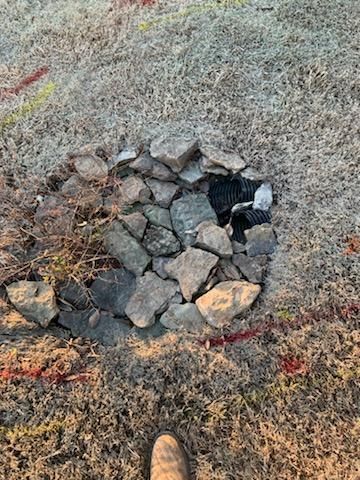 Pile of rocks surrounding a drainage outlet in dry grass, with red markings nearby.