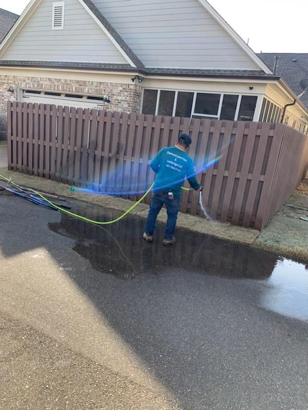Person power washing a brown wooden fence on a street, with water spraying.