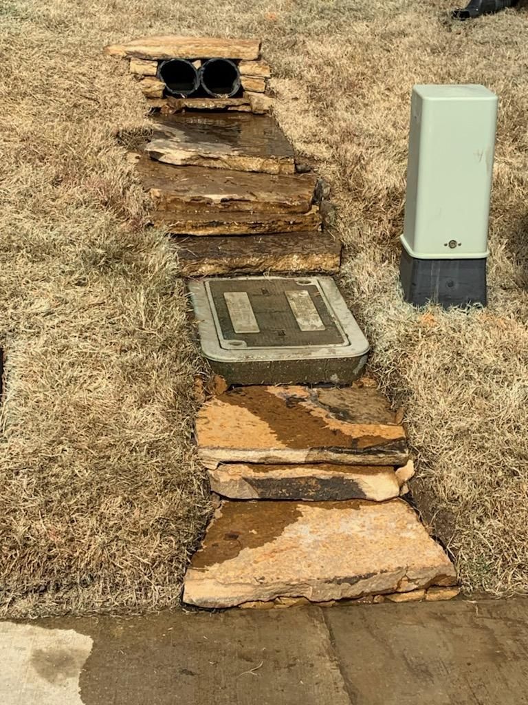 Stone steps leading up a small hill, with a utility box on the right and drainage pipes at the top.