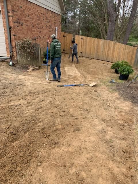 Two workers installing a fence in a backyard. One uses a post hole digger, the other works on the fence.