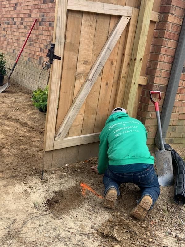 A man in a green sweatshirt is kneeling in the dirt next to a wooden gate.
