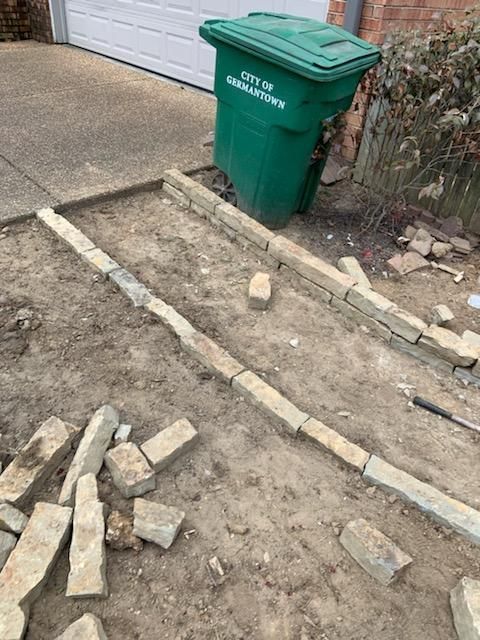 A green garbage can is sitting next to a pile of bricks.