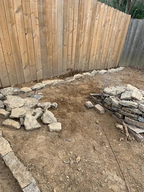 A pile of rocks is sitting in the dirt in front of a wooden fence.