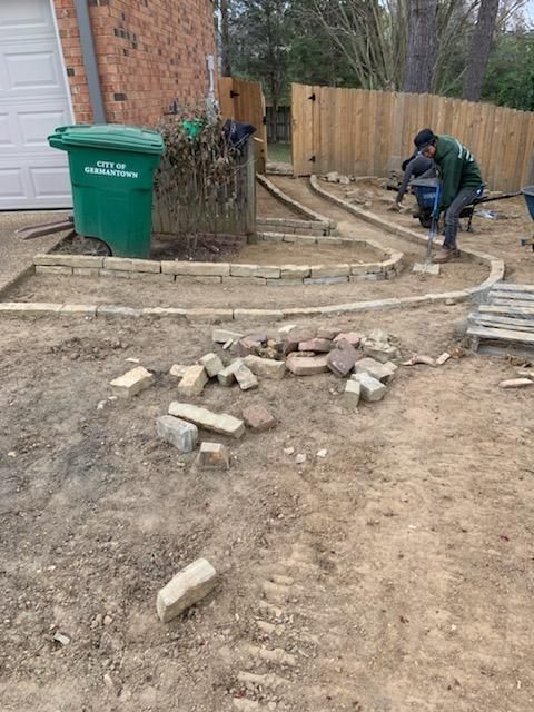 A man is working on a brick walkway in a backyard.