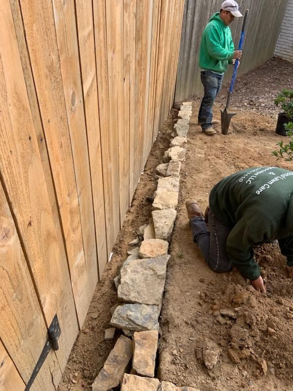 Two men are working on a stone wall next to a wooden fence.
