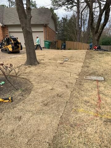 Construction site with a small tractor, worker, and exposed dirt next to a house.