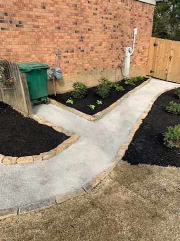 Concrete pathway splits, bordered by brick pavers and dark mulch, beside a brick wall.