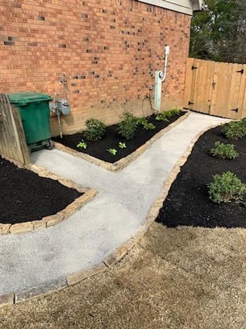 A concrete walkway leading to a brick house with a wooden fence.