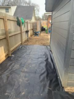 A backyard with a wooden fence and a black tarp on the ground.