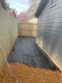 A backyard with a fence and a black tarp on the ground.