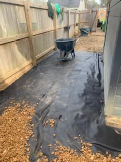 A wheelbarrow is sitting on top of a black tarp next to a wooden fence.