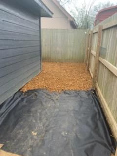 A backyard with a wooden fence and a black tarp on the ground.