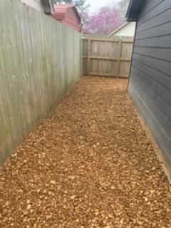 A backyard with a wooden fence and a pile of wood chips.