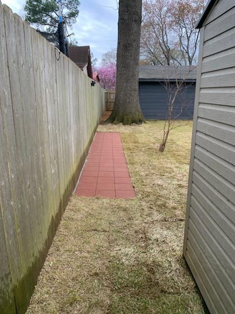 There is a red tiled walkway between a wooden fence and a shed.