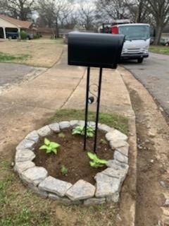 A black mailbox is sitting in the middle of a stone planter.