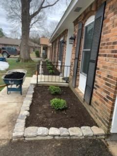 A wheelbarrow is filled with dirt in front of a brick house.