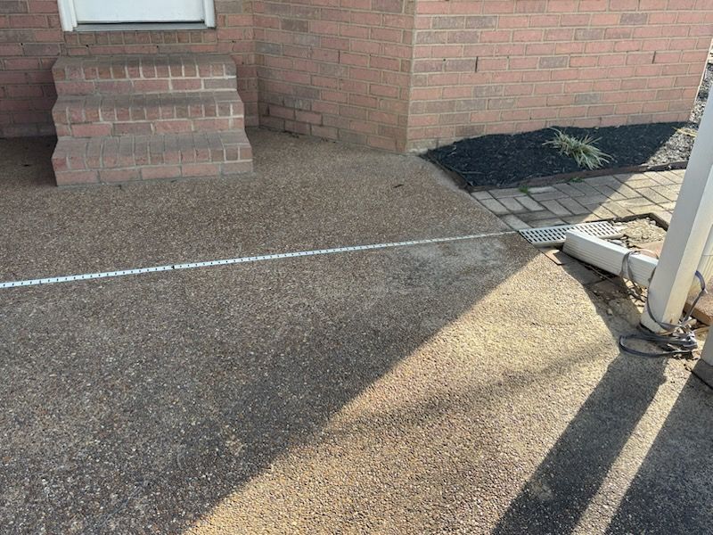 Brick home entrance with textured concrete pathway, leading to steps and a drainage channel.