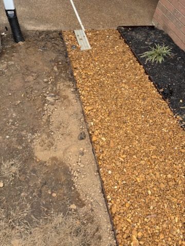 Gravel path between dirt and landscaped bed with a drain.