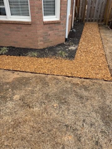 Wood chip pathway alongside a brick building and a wooden fence.