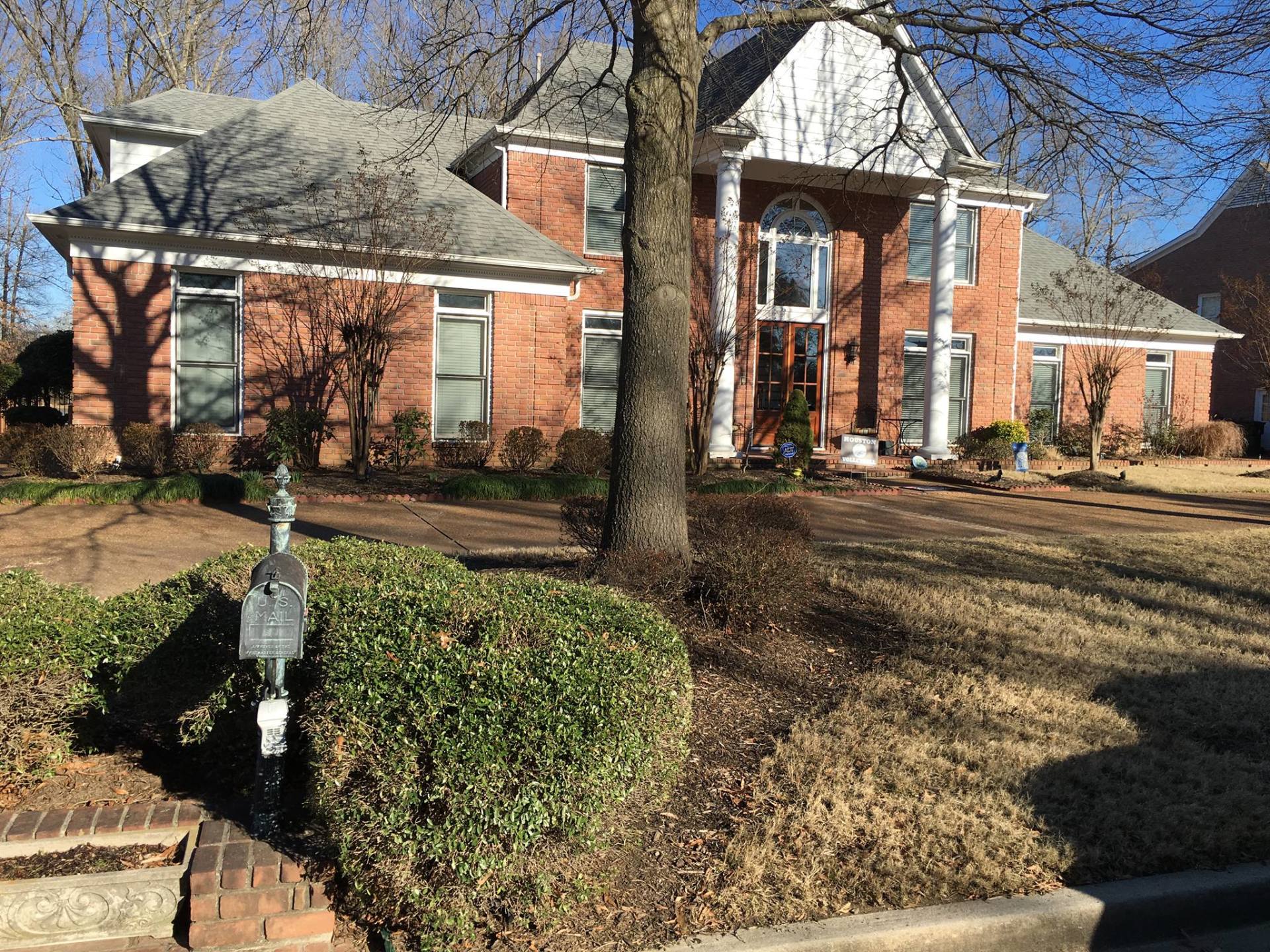 Two-story brick house with white columns, a large tree in front, and brown lawn.
