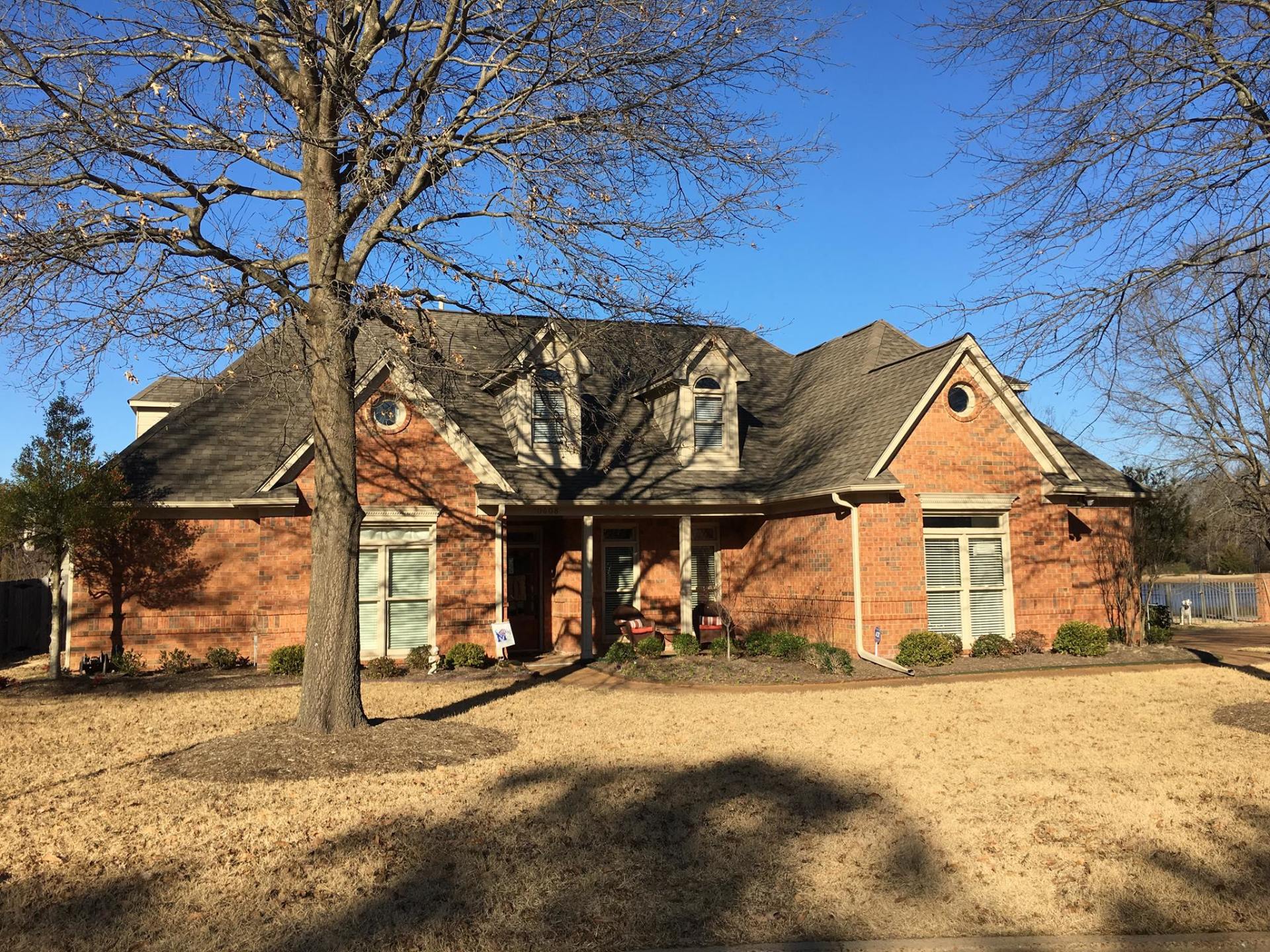 Red brick house with dark roof, bare tree in front, and clear blue sky.