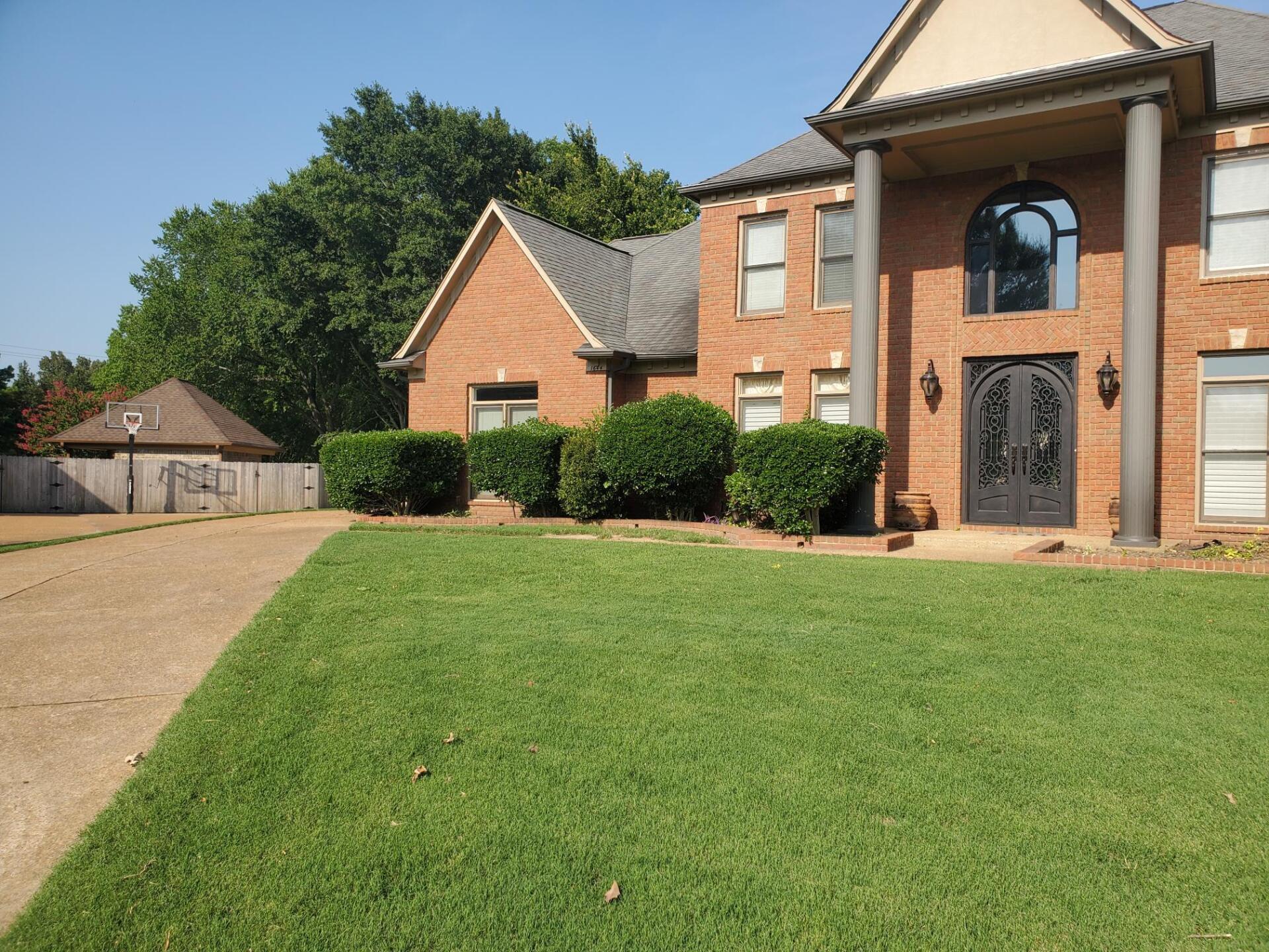 Brick house with a well-manicured lawn, driveway, and manicured shrubs.