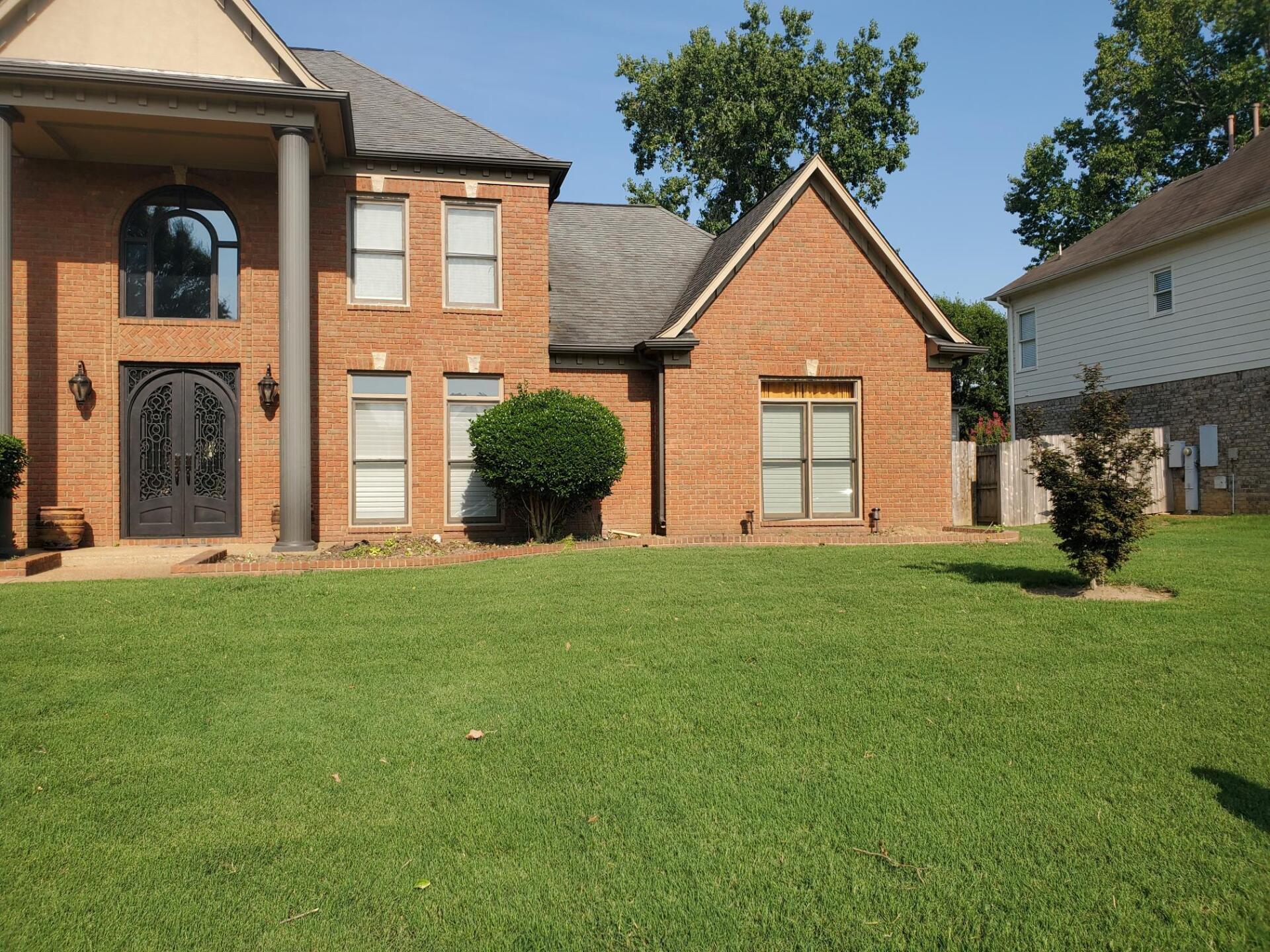 Brick house with a green lawn, large decorative front door, and a blue sky.
