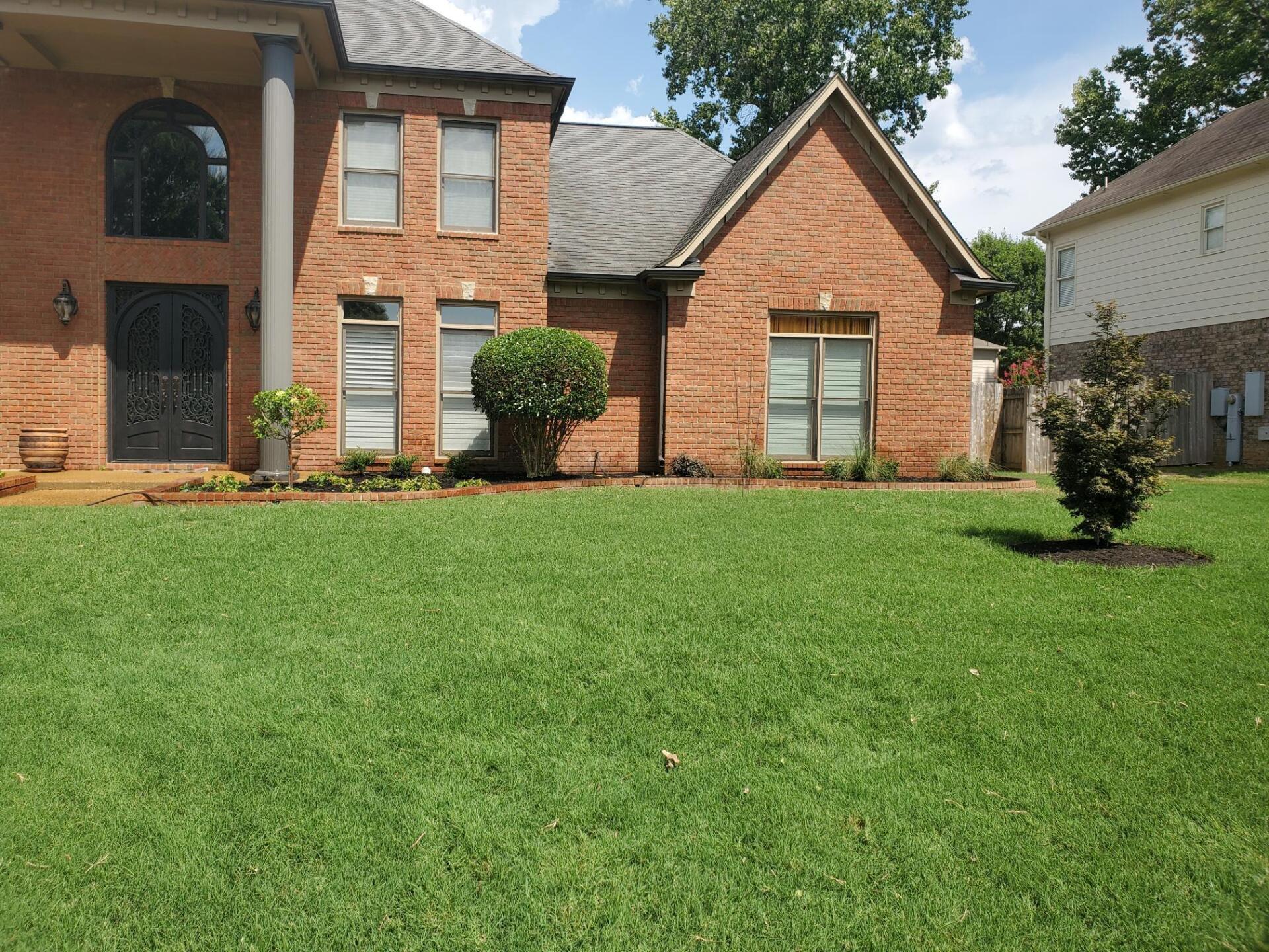 Two-story brick house with green lawn; front door with columns, windows, and landscaping.