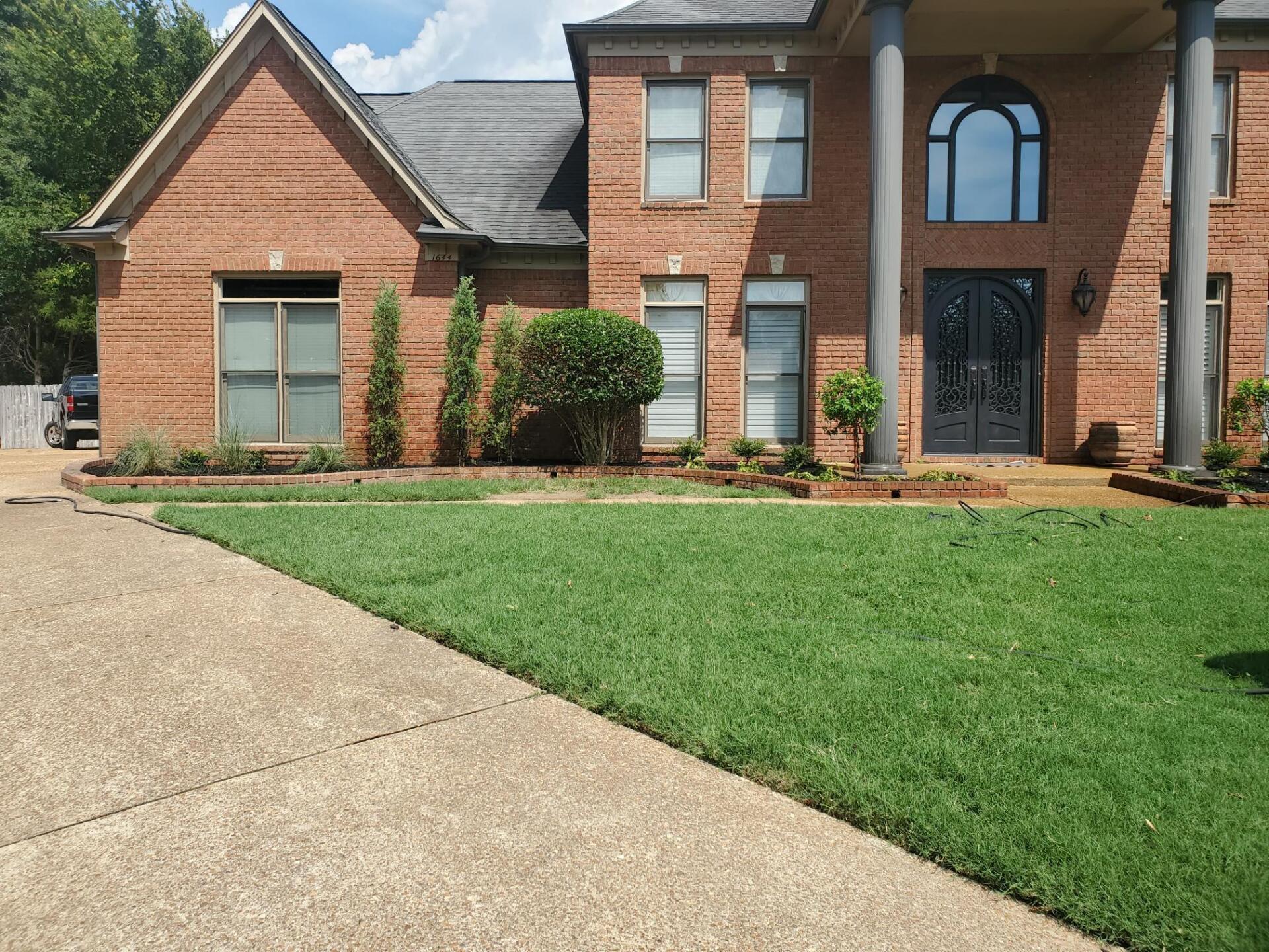 Brick house with green lawn, front porch, arched window, and driveway.
