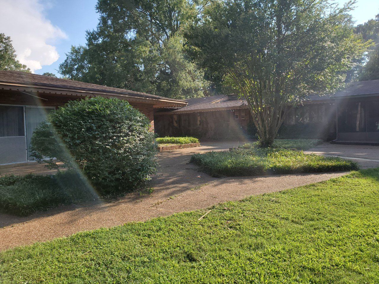 Exterior of a house with green lawn, gravel pathway, and garden beds with foliage; bright sunlight.