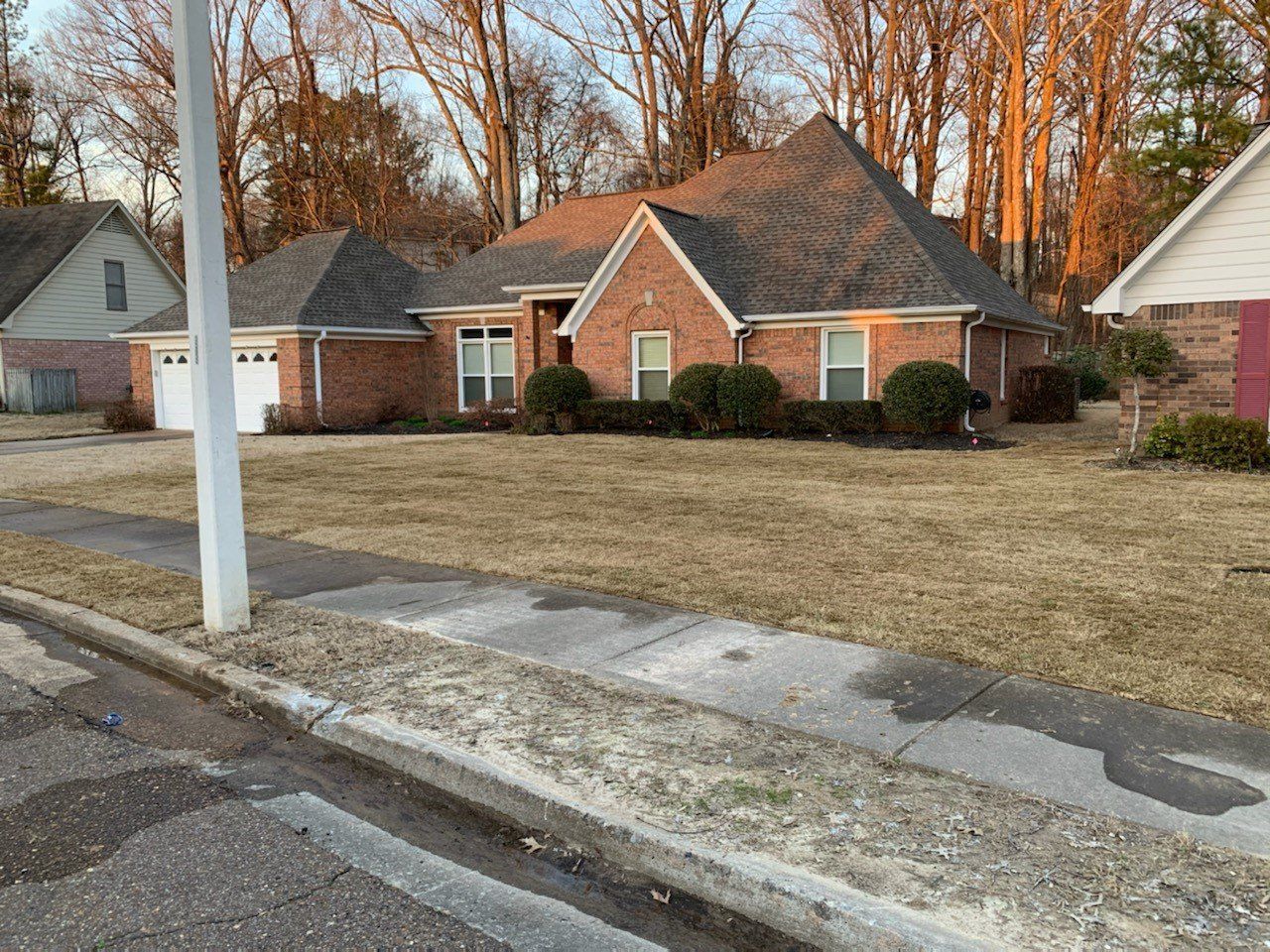 Brick house with brown roof and dry grass lawn on a sunny day.