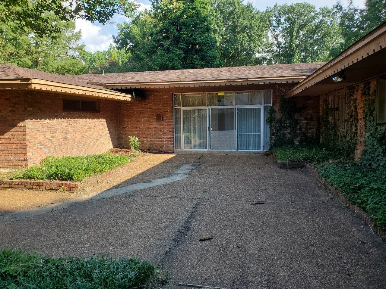 Brick house with gravel driveway; glass sliding doors; overgrown ivy.