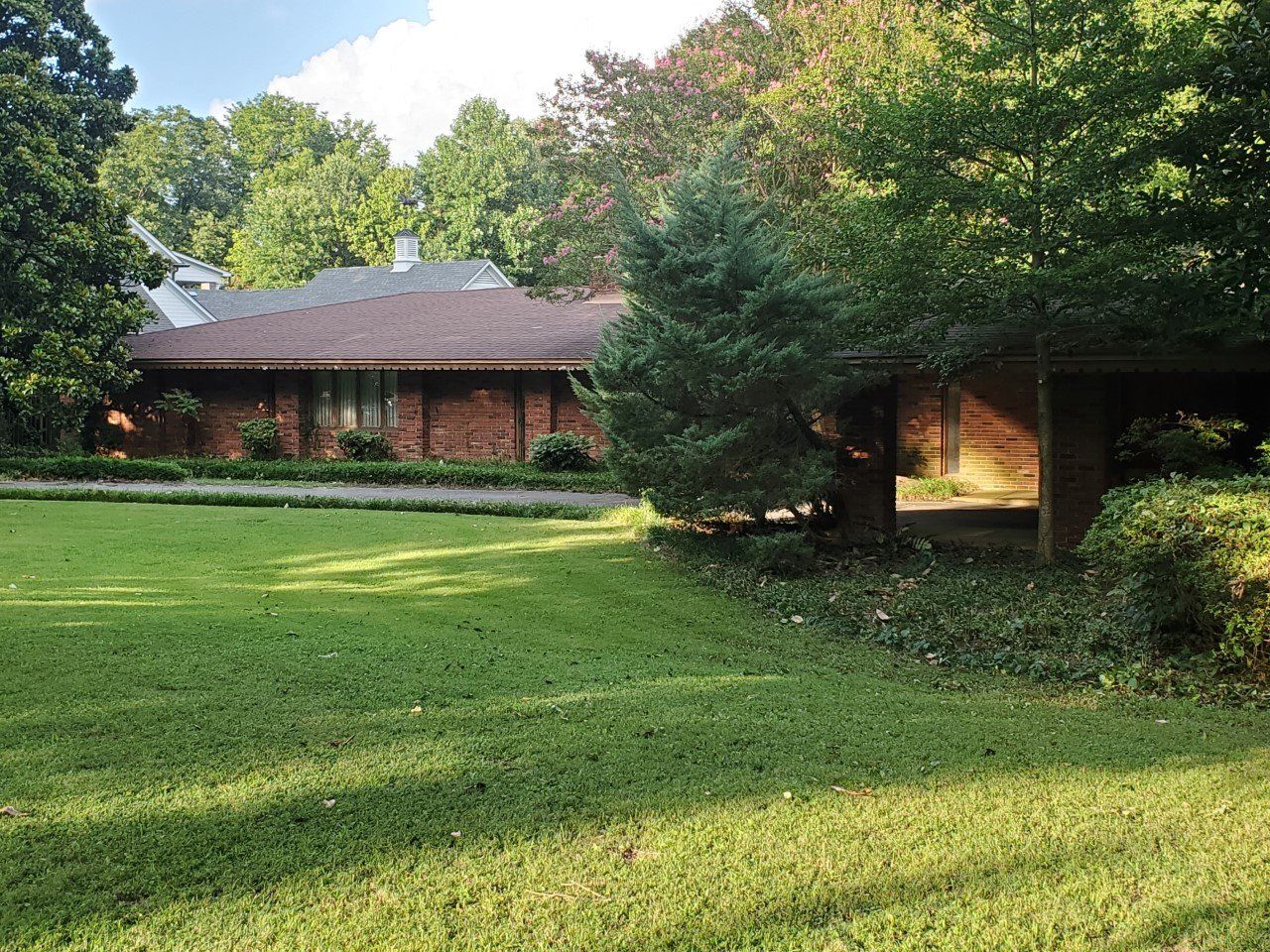 Brick house with brown roof, green lawn and trees.