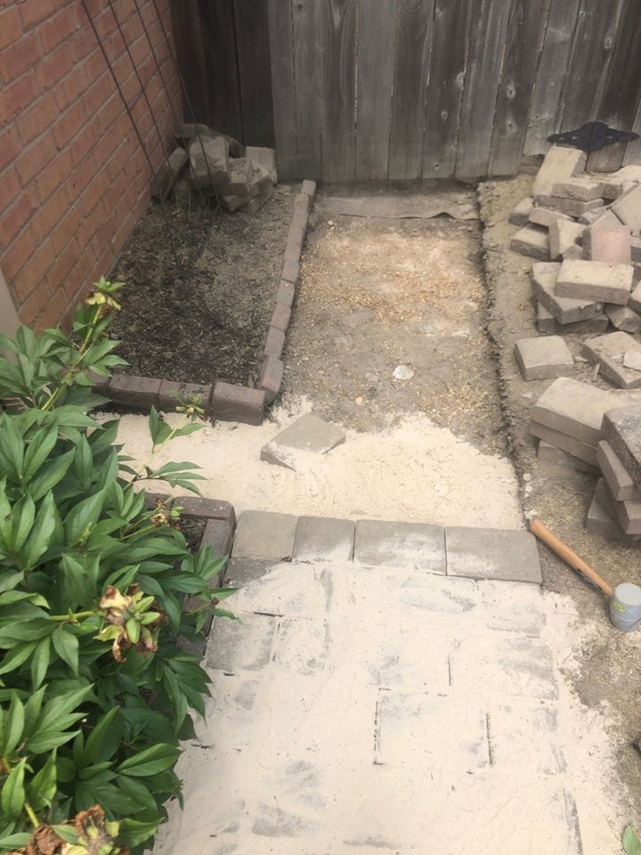 Brick pavers being laid for a pathway in a yard, near a fence and building.