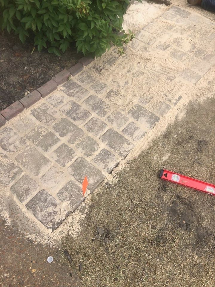 Brick pathway being repaired with sand, red level, and orange flag in the foreground.