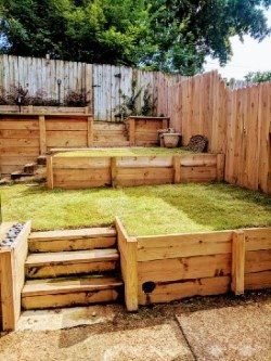 Wooden terraced backyard with steps and retaining walls, filled with grass and plants.