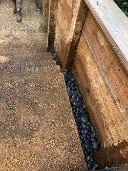 Wooden retaining wall next to brown concrete steps, black pebbles in between.
