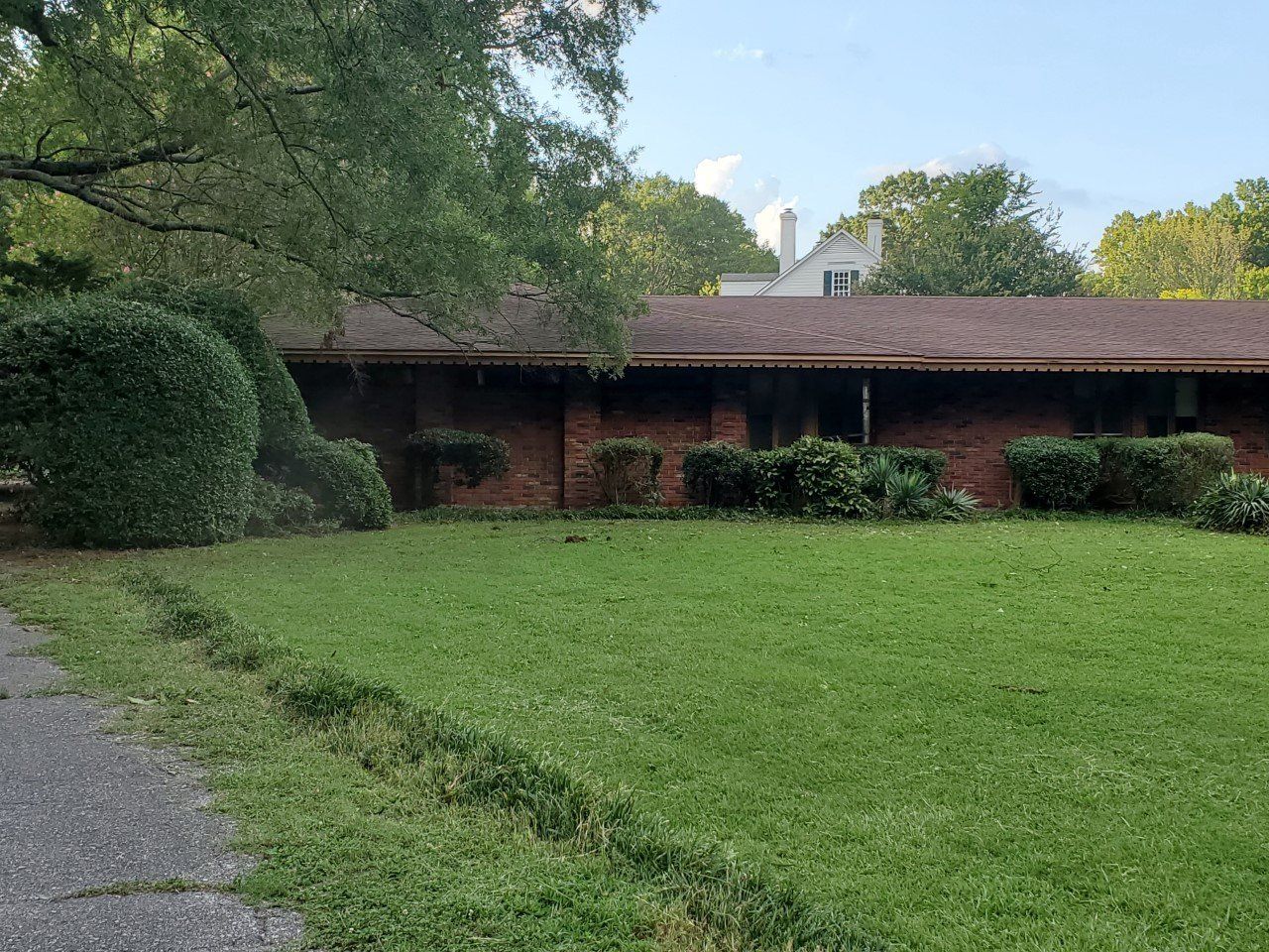 A brick house with a brown roof and green lawn and bushes in front.
