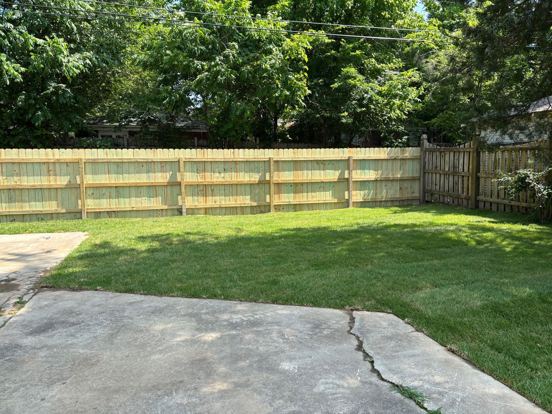 Backyard with a wooden fence, green grass, and a concrete patio.
