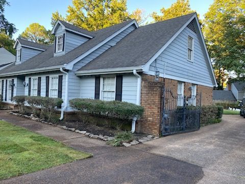 Blue house with black shutters, brick accents, and a driveway.