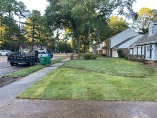 Lawn with newly laid sod, a truck with a trailer, and houses on a sunny day.