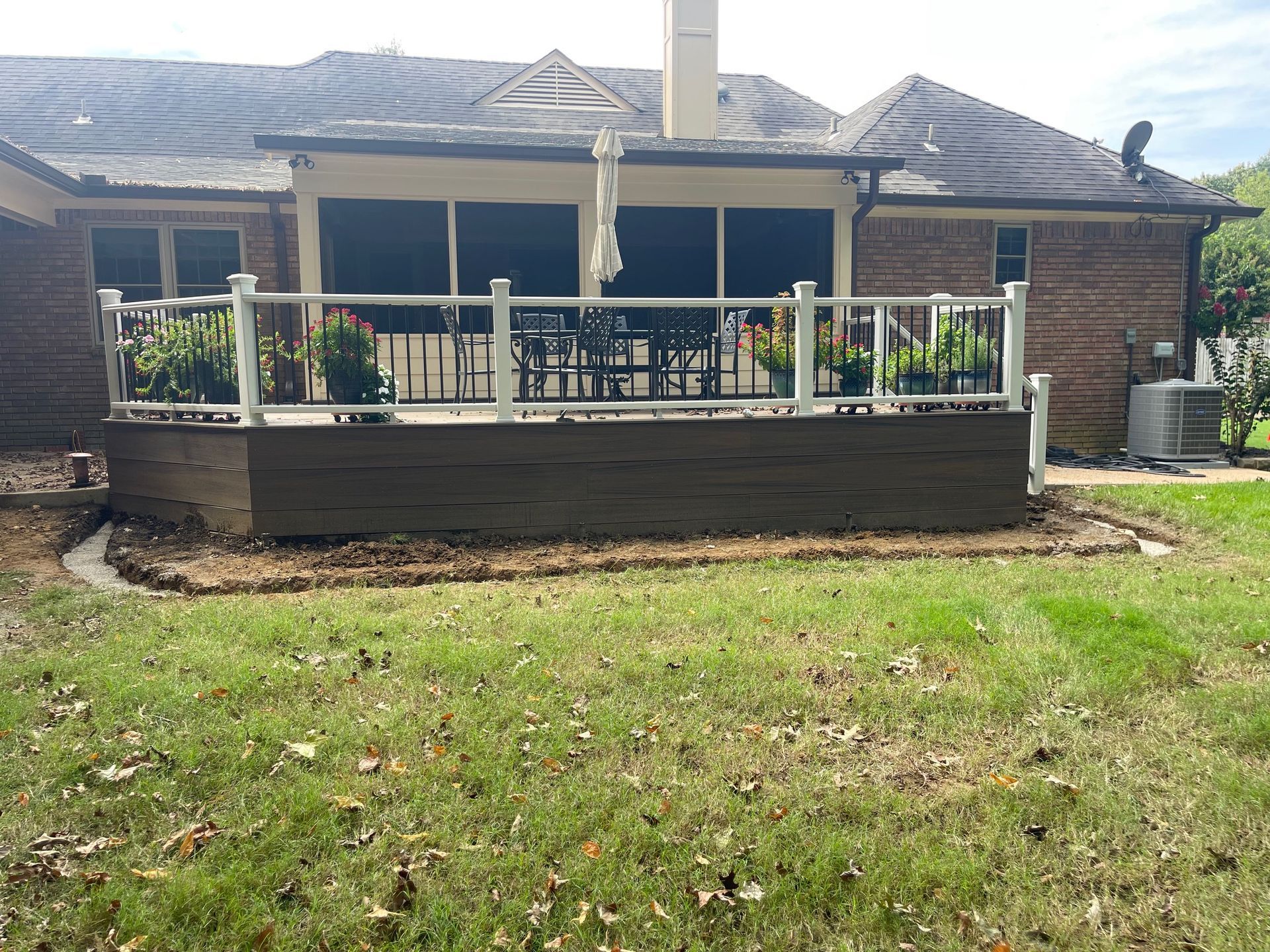 Backyard deck with brown composite boards, white railing, and green plants against a brick house.
