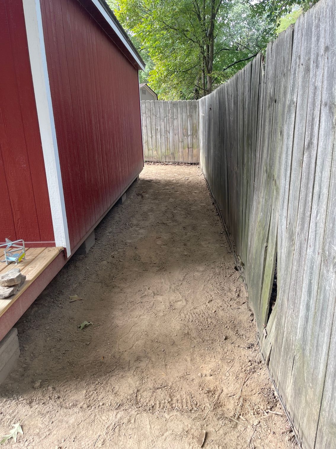 Narrow dirt path between a red shed and a wooden fence.