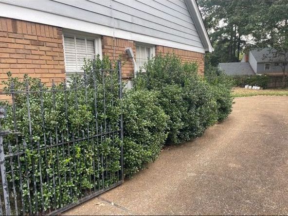 Brick house with line of green bushes and black wrought iron fence along concrete driveway.