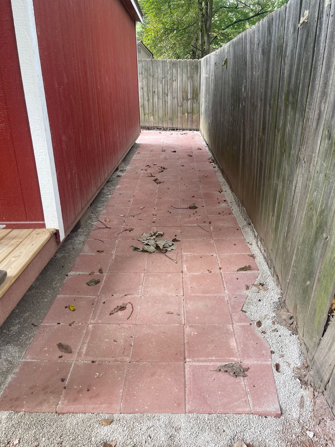 Brick path between a red shed and a weathered wooden fence.