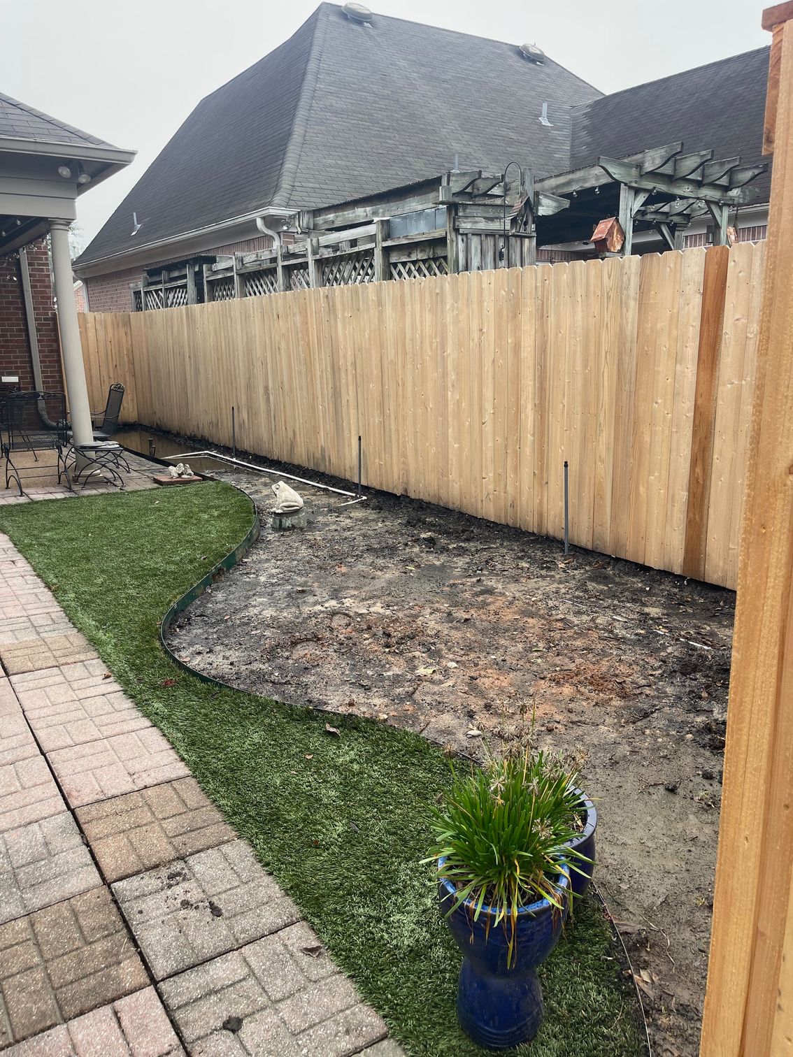 Backyard with a new wooden fence, artificial turf, and dirt awaiting landscaping.
