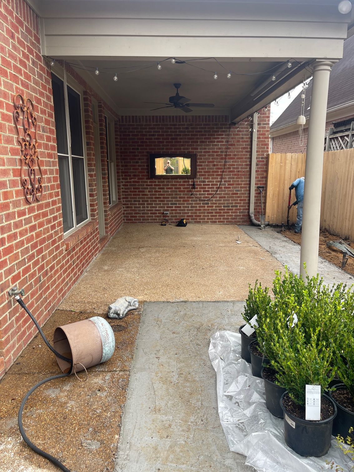 Brick patio with pea gravel floor; TV on wall; potted plants and hose present.