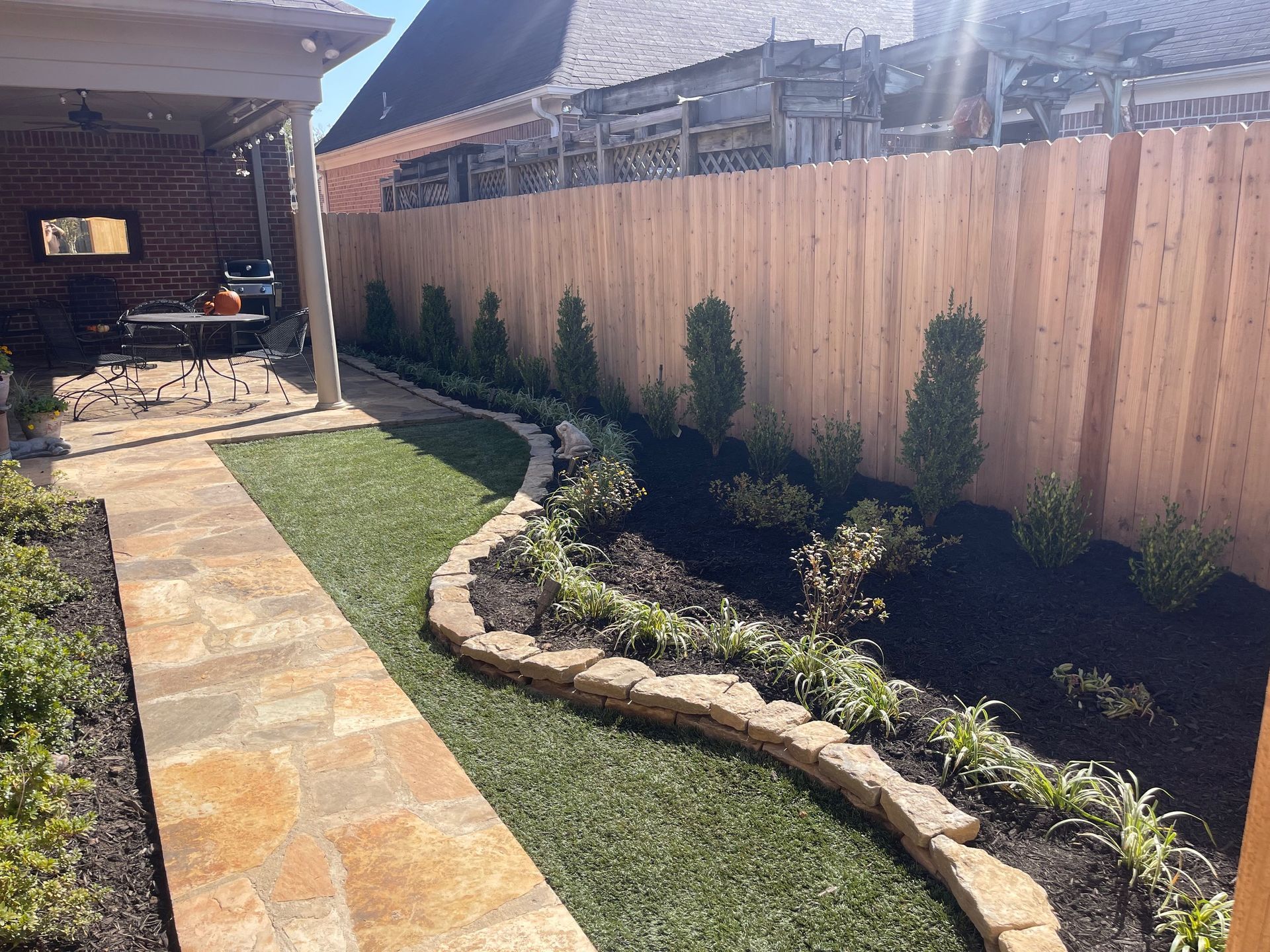 Backyard path with stone pavers, bordered by a rock garden, artificial turf, and wooden fence.